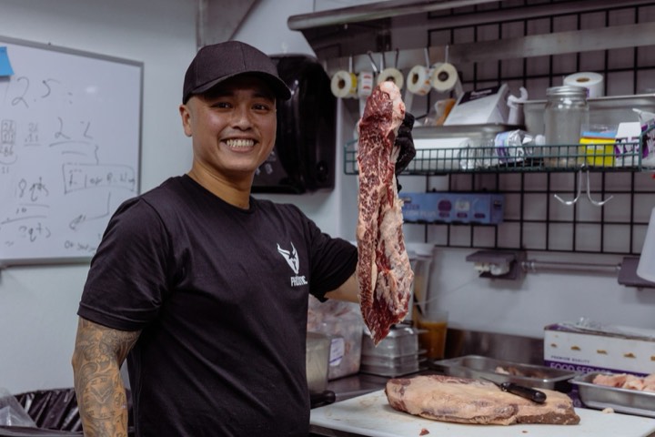 Hai Le smiling in the PhoXotic kitchen beside a hanging strip of beef