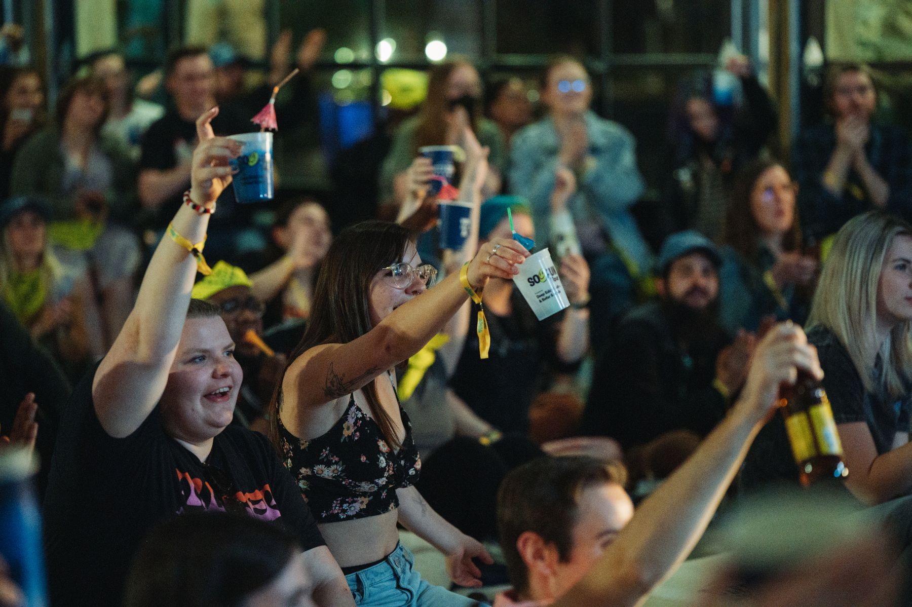 A packed warehouse crowd cheering and raising their cups